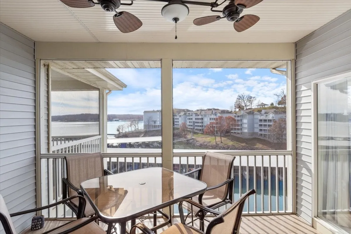 A bright, airy room with a table and chairs under a ceiling fan, positioned to maximize views of the lake through large windows. The space exudes relaxation, offering an ideal setting for morning coffee or family meals with a scenic water backdrop.