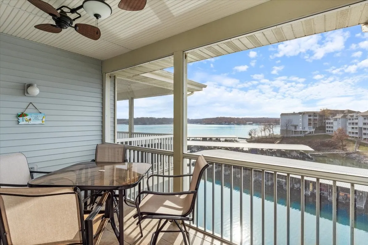An outdoor dining table set under a ceiling fan, with panoramic lake views providing a serene backdrop. The space is styled for comfort and conversation, ideal for al fresco meals or leisurely afternoons by the water.