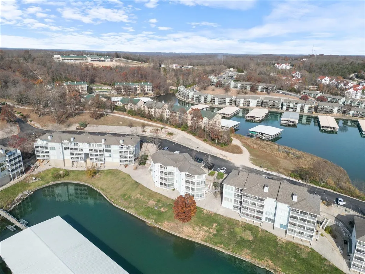 A stylish exterior view of the waterfront with modern buildings, a marina, and lush surrounding nature. The inviting shoreline is perfect for strolls, boating, or finding quiet moments together amidst the upscale Regatta Bay community.