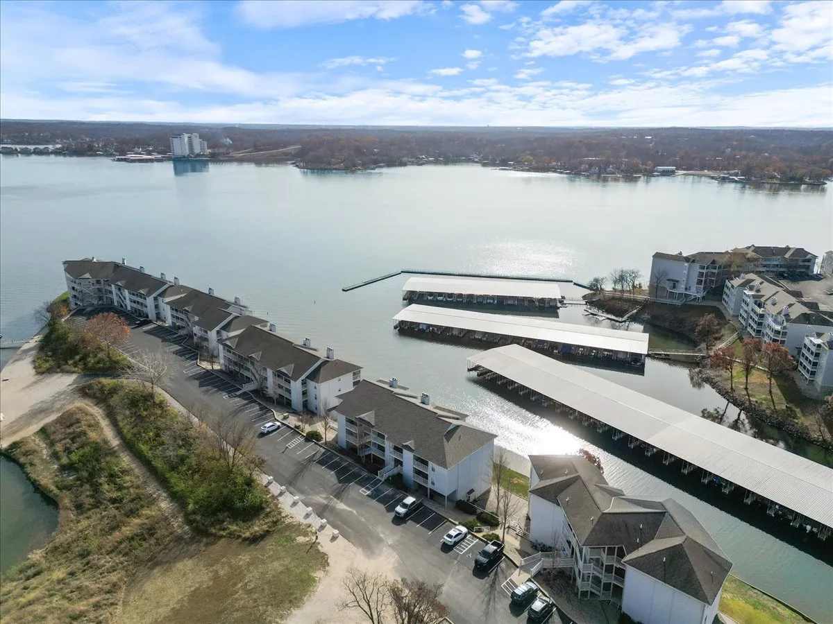 This exterior image captures a vibrant waterfront view, featuring a marina with boats, residential buildings, and a spacious parking lot. The scene is alive with the energy of boating, fishing, and people walking by the water, all set against the tranquil backdrop of the lake.