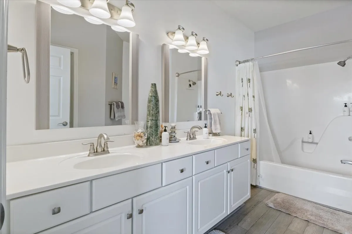 A spacious, modern bathroom featuring a double vanity with sinks, large mirrors, and a bathtub. The neutral tones and clean lines evoke a refreshing and serene atmosphere, perfect for morning routines or relaxing baths.