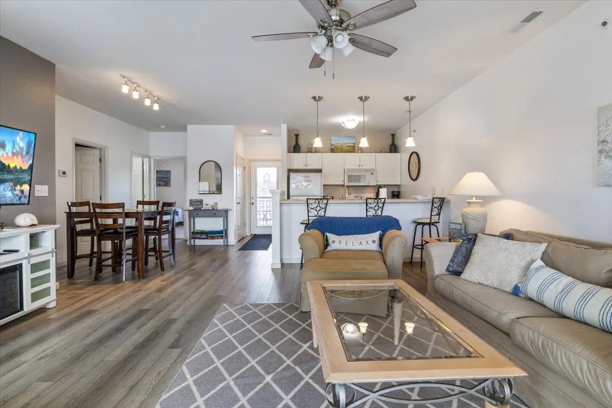 This image presents a spacious open-concept area that seamlessly includes a comfortable sofa, coffee table, dining space, and a modern kitchen. The area is designed for both relaxation and gatherings, with tasteful decor and ample space for group activities.
