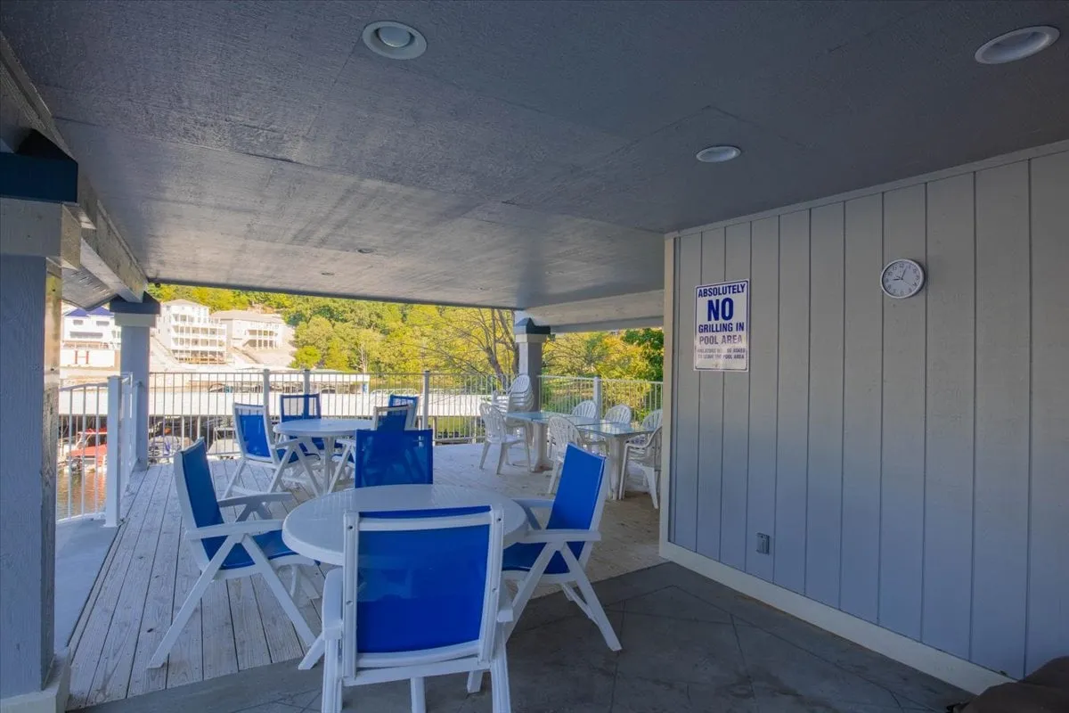A casual, inviting screened-in deck furnished with blue and white chairs and tables. The scene is set for social gatherings, relaxation, or simply enjoying the gorgeous sunset views over the water. Signage adds a personalized, welcoming touch to the space.